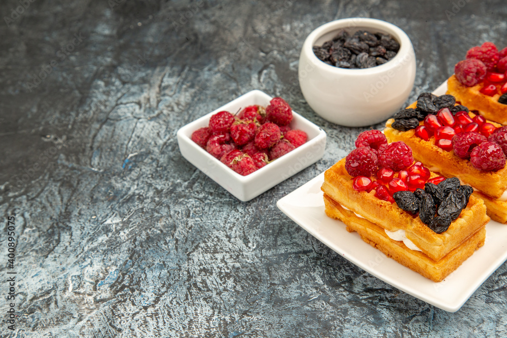 bottom view berry waffles on white rectangular plate bowls of raisins and raspberries on grey-white background with copy space bottom view berry waffles on white rectangular plate bowls of raisins and raspberries on grey-white background with copy space