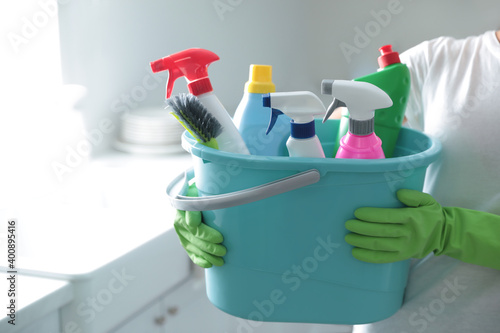 Woman holding bucket with cleaning supplies in kitchen, closeup