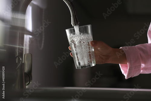 Woman pouring water into glass in kitchen, closeup