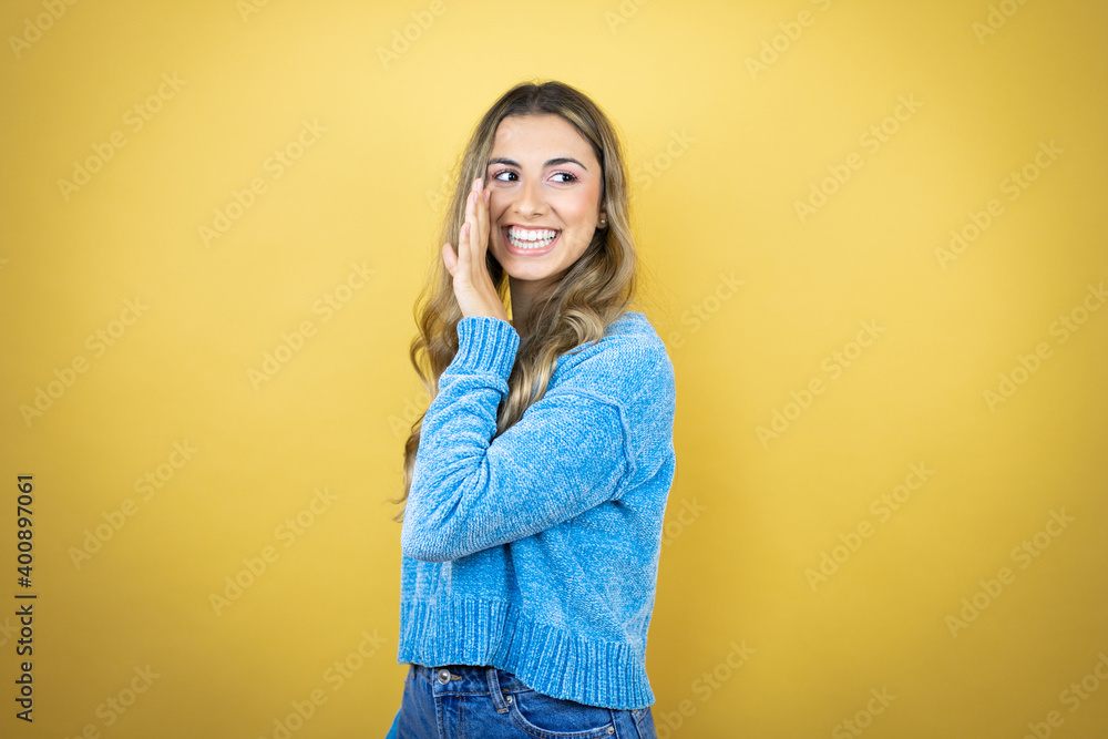 Pretty blonde woman with long hair standing over yellow background with hand on mouth telling secret rumor, whispering malicious talk conversation Pretty blonde woman with long hair standing over yellow background with hand on mouth telling secret rumor, whispering malicious talk conversation