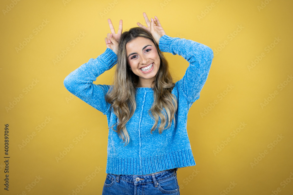 Pretty blonde woman with long hair standing over yellow background Posing funny and crazy with fingers on head as bunny ears, smiling cheerful Pretty blonde woman with long hair standing over yellow background Posing funny and crazy with fingers on head as bunny ears, smiling cheerful