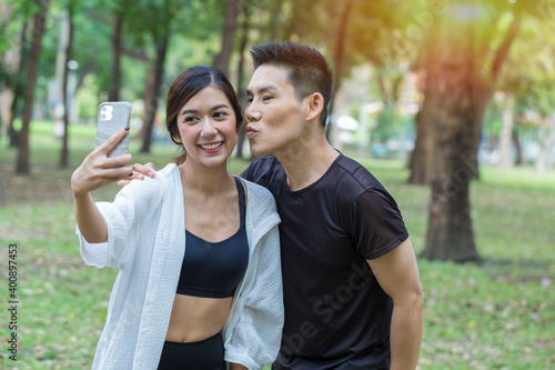 Asian couple wearing sportswear, running in the morning at park and use smart phone selfie together.Sport and health concept.