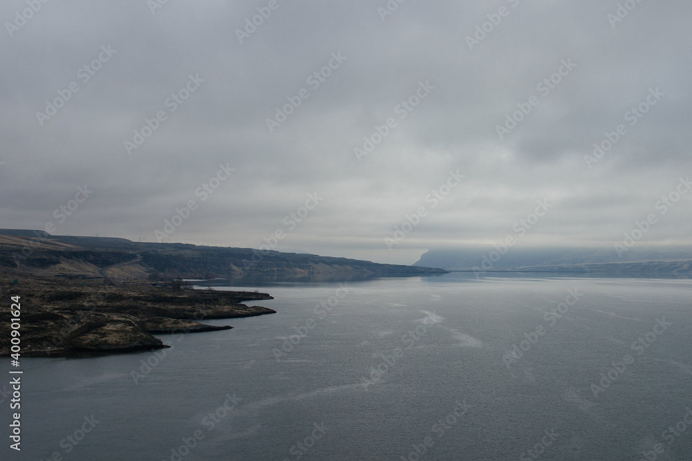 Obraz premium A beautiful foggy landscape in a blue-gray scale: a wide river, in front of the horizon are dark blue mountains, on the banks of the hills with dry grass. Colorado river, OR, USA