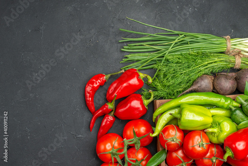 Horizontal view of vegetable basket with a bunch of green and peppers cucumber and tomatoes with stem carrots beets on dark background
