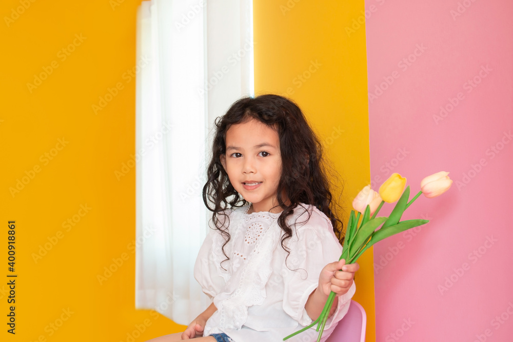 Little kid girl holding tulips flower sitting bar chair. Cute asian little girl happy playing and smiling at living room. Copy space for text. Little kid girl holding tulips flower sitting bar chair. Cute asian little girl happy playing and smiling at living room. Copy space for text.