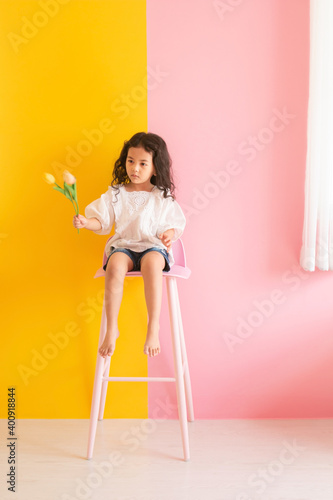 Little kid girl holding tulips flower sitting bar chair. Cute asian little girl happy playing and smiling at living room. Copy space for text.