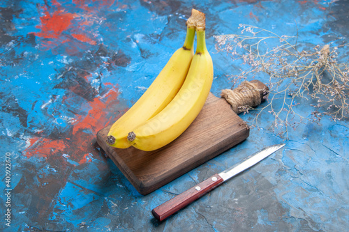 Vertical view of a wooden tray with fresh natural cavendish bananas and knife on isolated blue background photo