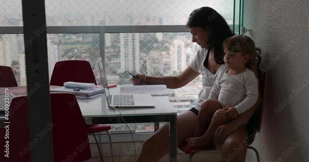 Mother multi-tasking at home, infant toddler boy watching cartoon on laptop while mom studying Mother multi-tasking at home, infant toddler boy watching cartoon on laptop while mom studying
