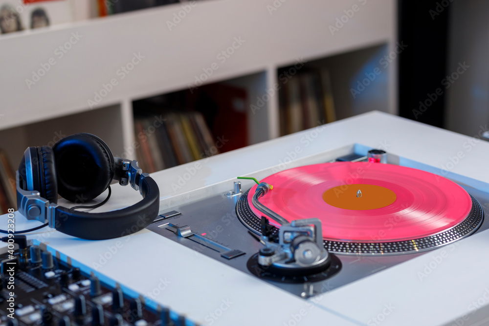 Foto Stock Mesa de Dj con un tocadiscos que tiene un disco de vinil rosa y  unos audífonos al costado. Concepto de música retro