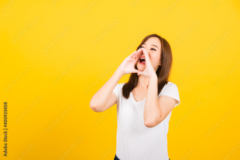 Asian happy portrait beautiful cute young woman teen standing big shout out with hands next mouth giving excited positive looking to side isolated, studio shot on yellow background with copy space Asian happy portrait beautiful cute young woman teen standing big shout out with hands next mouth giving excited positive looking to side isolated, studio shot on yellow background with copy space