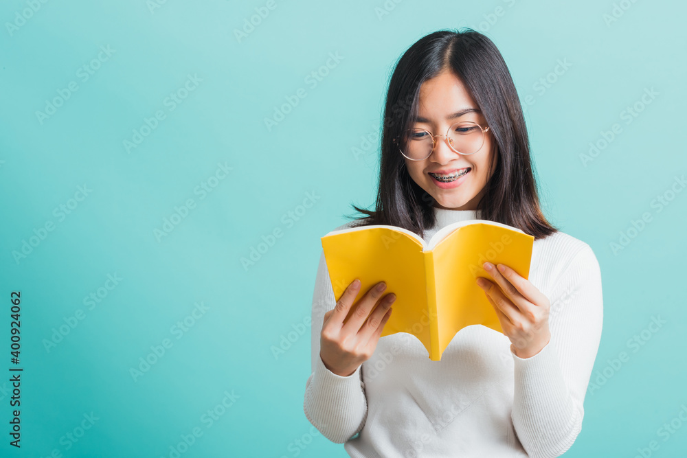 Portrait female in glasses is holding and reading a book, Young beautiful Asian woman hiding behind an open book, studio shot isolated on a blue background, Education concept Portrait female in glasses is holding and reading a book, Young beautiful Asian woman hiding behind an open book, studio shot isolated on a blue background, Education concept