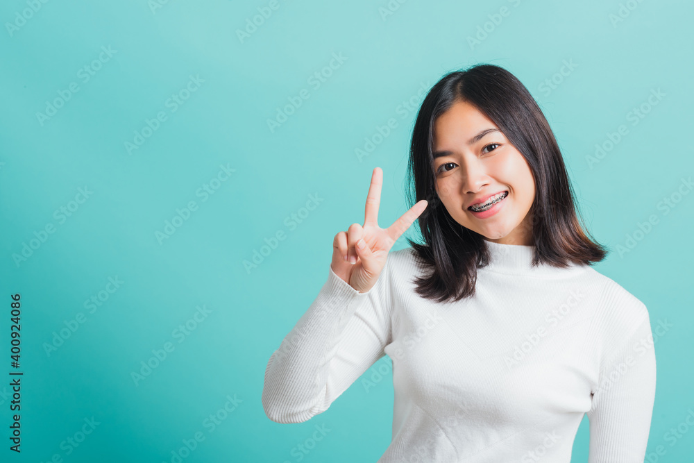 Portrait female give V-sign near-eye make Hollywood white smile, Young beautiful Asian woman showing peace gesture victory, studio shot isolated on a blue background Portrait female give V-sign near-eye make Hollywood white smile, Young beautiful Asian woman showing peace gesture victory, studio shot isolated on a blue background