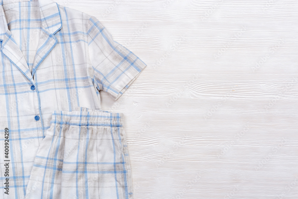 Folded warm white pajamas with blue checks or stripes on white wooden background Folded warm white pajamas with blue checks or stripes on white wooden background