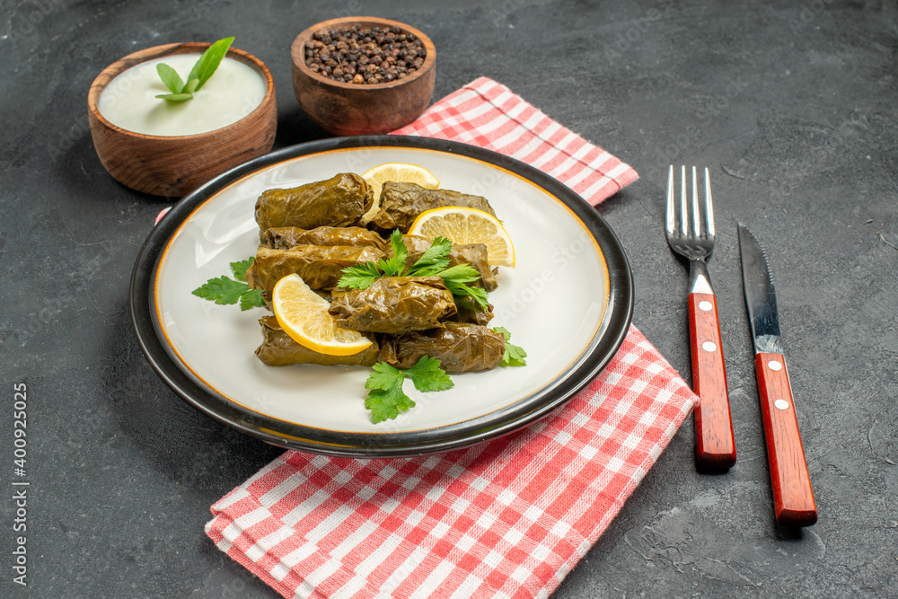 bottom view stuffed grape leaves on white plate bowls of natural yogurt and black pepper knife and fork napkin on dark background bottom view stuffed grape leaves on white plate bowls of natural yogurt and black pepper knife and fork napkin on dark background