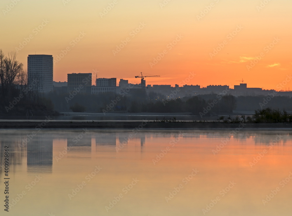 Golden sunrise on the banks of the Ob River. City houses and trees on the shore