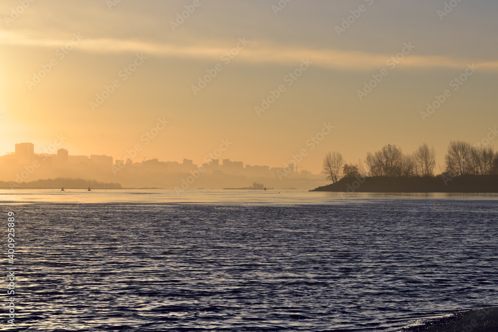 Golden dawn over the river Ob. The trees and the city of Novosibirsk appear from the fog on the horizon Golden dawn over the river Ob. The trees and the city of Novosibirsk appear from the fog on the horizon