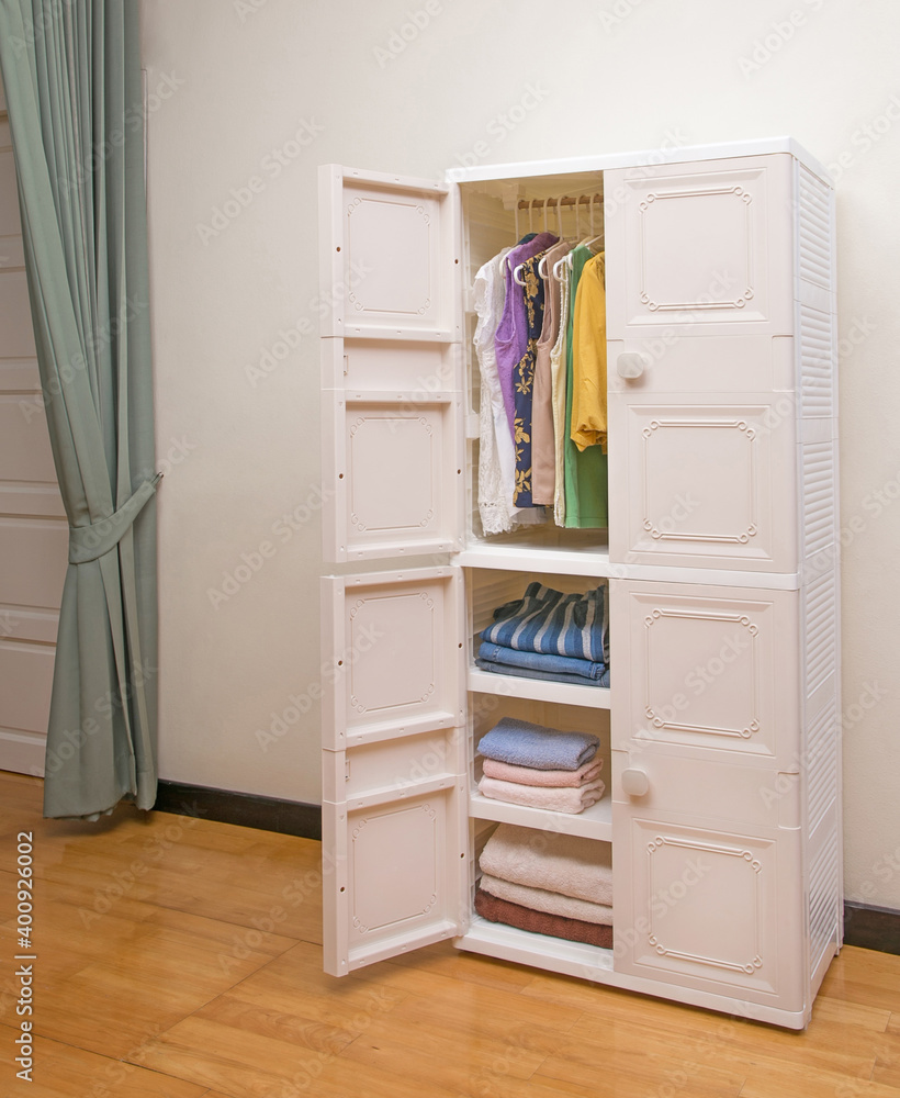 Opened plastic wardrobe with clothing in bedroom