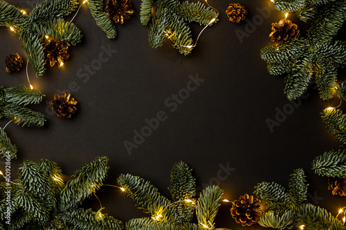 garland of fir branches and cones and lights on a black background with copy space