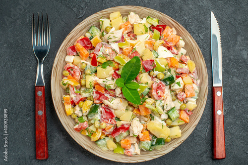 top close view of bowl of vegetable salad with fork and knife on side on dark grey background