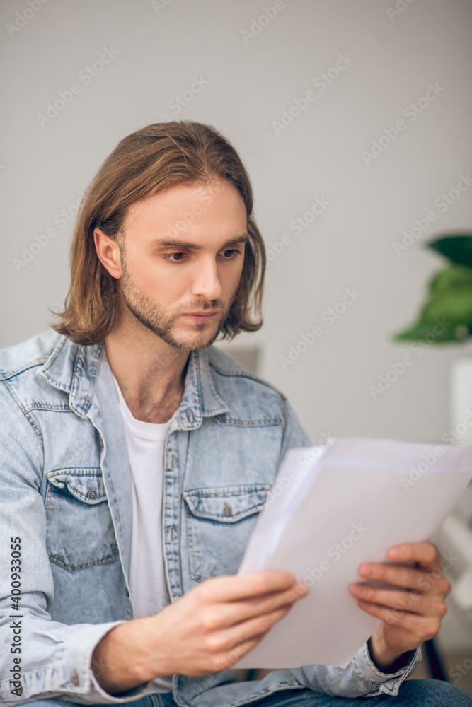 Young man in jeans shirt holding papers and looking serious