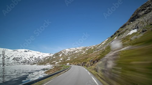 A drive on the narrow road along the Langvatnet to the Geiranger. The lake is still partly frozen, snow covering the hills and hilltops. Cars and camping cars following the road. photo