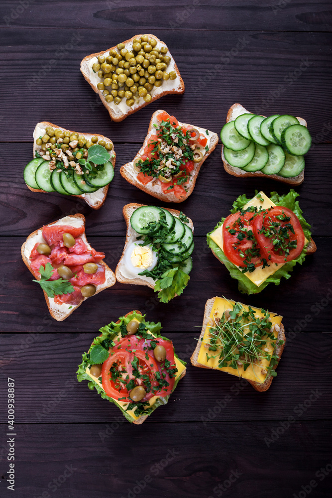 Toasts, sandwiches with cream cheese, cucumbers, tomatoes, salmon, sprouts, egg on a brown wooden background. Healthy food concept. overhead.
