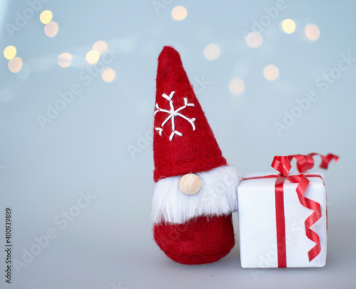 Christmas gnome with a gift. New Year. Symbol of Christmas. christmas  light. bokeh. red and white.christmas card. fairy tail. snowflake, cap. soft toy. copy space. © masianya