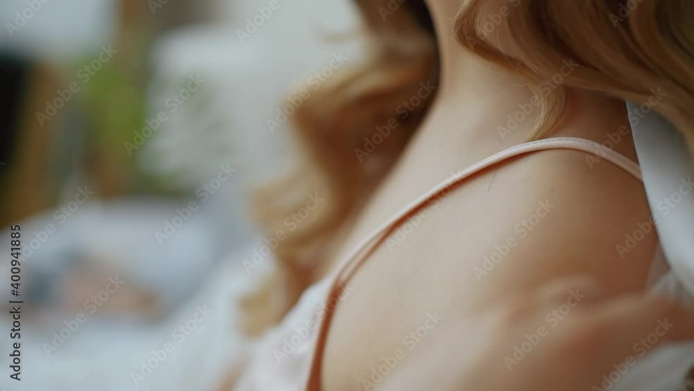 Close-up, caucasian girl with curls in a peignoir bares her shoulders, taking off her lace robe