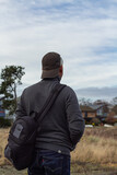 Back view of the man with backpack stands in the field and looks into the distance.