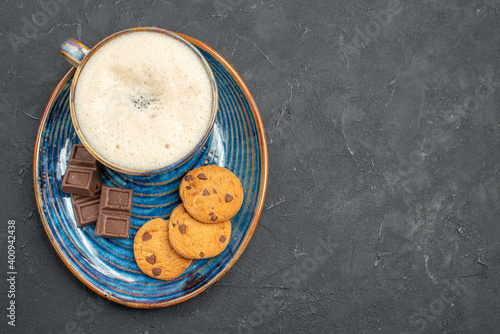 Above view of delicious breakfast with a cup of milk biscuits and chocolate bars on blue tray on dark background
