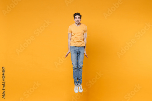 Full length side view of young overjoyed caucasian excited fun happy surprised man 20s wearing casual t-shirt jeans high jumping up looking camera isolated on yellow color background studio portrait.