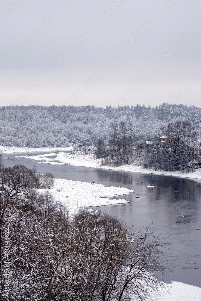 A powerful dark river flows among snow-covered banks covered with forests.