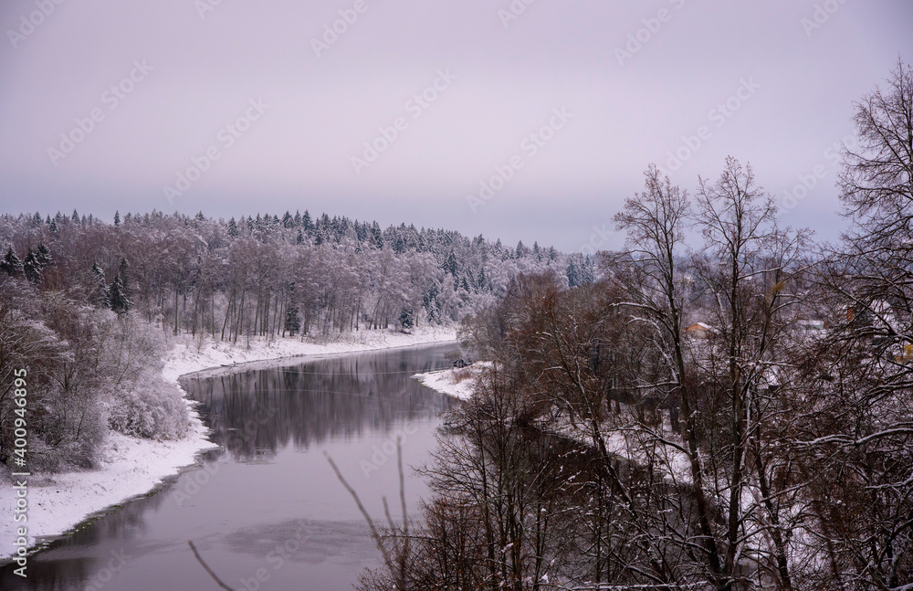 A powerful dark river flows among snow-covered banks covered with forests.