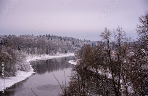 A powerful dark river flows among snow-covered banks covered with forests.