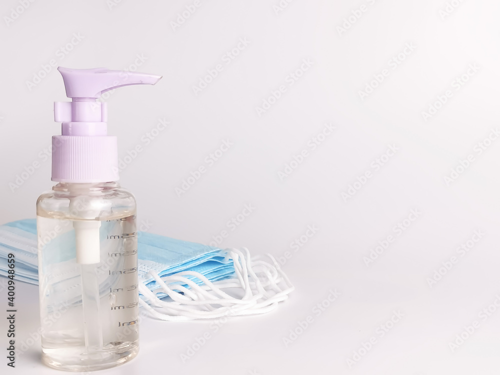 White background with a bottle of hand sanitizer and a bunch of disposal face mask. Selective focus.Medical concept. White background with a bottle of hand sanitizer and a bunch of disposal face mask. Selective focus.Medical concept.