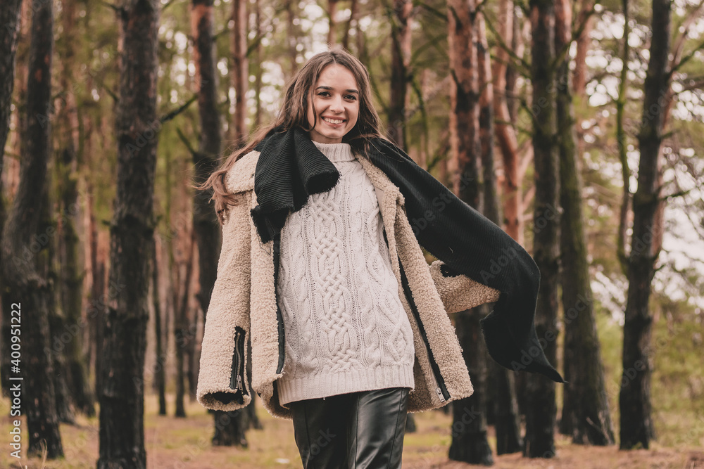 a woman of model appearance with long dark hair holds a scarf in her hands and smiles while in a pine forest a woman of model appearance with long dark hair holds a scarf in her hands and smiles while in a pine forest