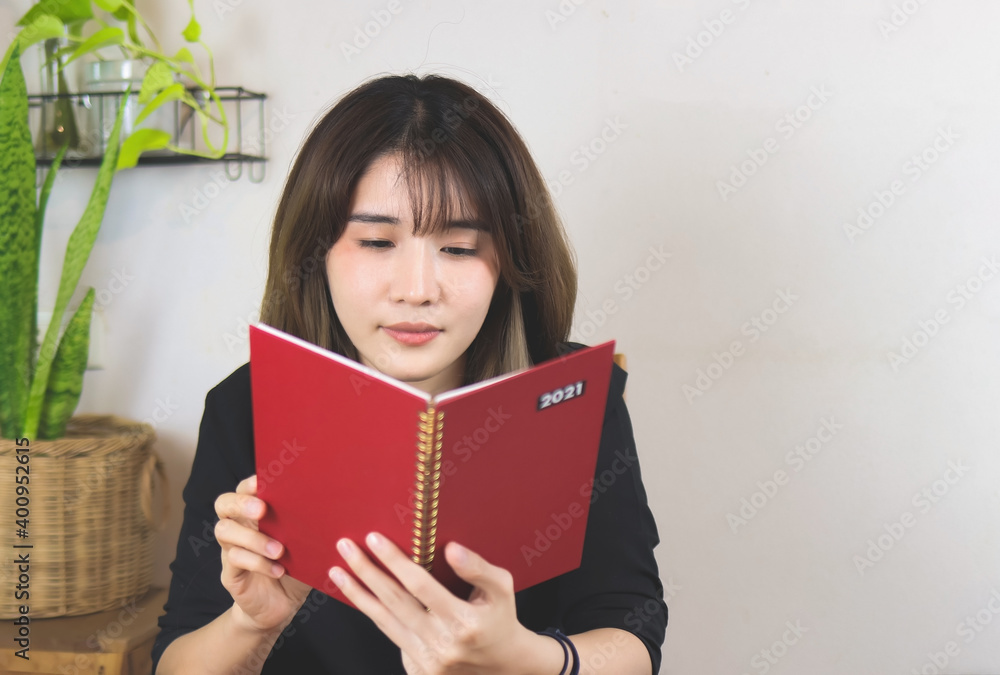 Asian woman open red 2021 diary, smiling . white wall with house plant background. Asian woman open red 2021 diary, smiling . white wall with house plant background.