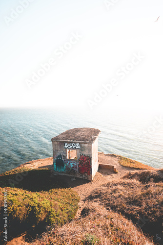 Fototapet Abandoned bunker on rocky coastline at sunset