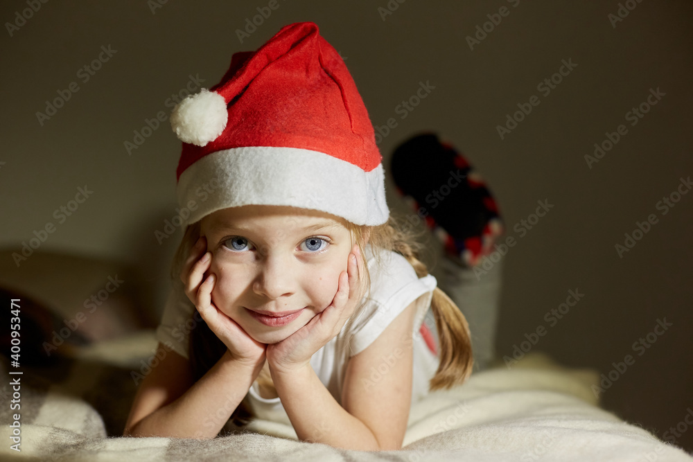 little happy girl in a santa claus hat waiting for Christmas gifts, portrait of a girl, a child looks into the camera lens little happy girl in a santa claus hat waiting for Christmas gifts, portrait of a girl, a child looks into the camera lens