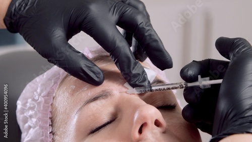 Doctor's hands in protective medical black gloves make injections hyaluronic acid into the female face. Face mesotherapy procedure in a beauty salon. Biorevitalization. Cosmetology.