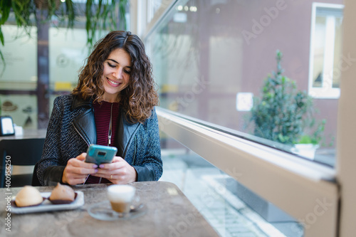 Copy scape close-up attractive young caucasian woman portrait sitting in a cafe with cup pf coffee and pastries. Smiling cheerful girl using smartphone.
