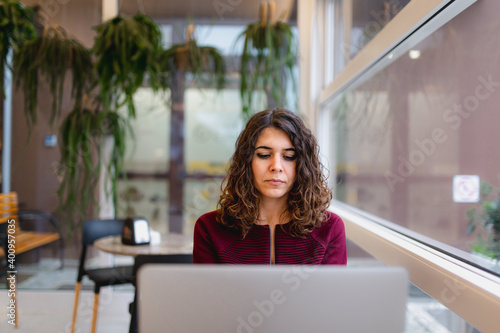 Close-up portrait of young woman in a cafe sitting in a table using computer laptop with serious face absorbed in her work.