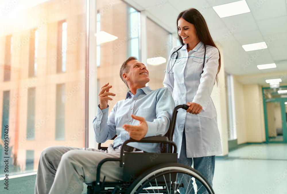 Caucasian beautiful nurse taking care of a mature male patient sitting in a wheelchair at the hospital. The woman smiles at the elderly man. Caucasian beautiful nurse taking care of a mature male patient sitting in a wheelchair at the hospital. The woman smiles at the elderly man.