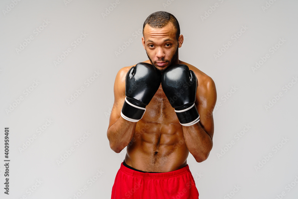 Confident young African boxer in boxing gloves standing over light grey background
