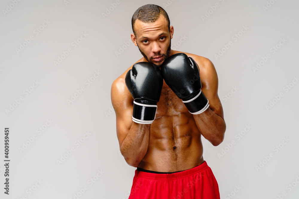 Confident young African boxer in boxing gloves standing over light grey background