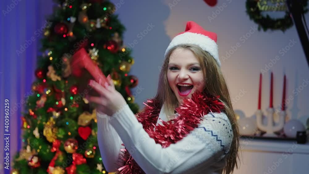 A Caucasian woman is turning in slow motion and showing the wrapping of a Christmas present in a cozy decorated room near a Christmas tree. Getting ready for the New Year holiday. A Caucasian woman is turning in slow motion and showing the wrapping of a Christmas present in a cozy decorated room near a Christmas tree. Getting ready for the New Year holiday.