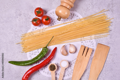 Red cherry tomato with peper mill and wooden spoon garlic origan and red and green paprika with spaghetti