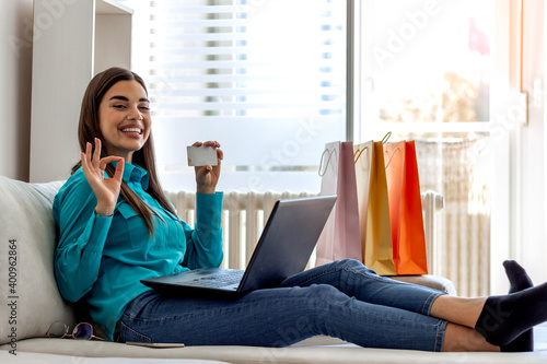 Young woman buying presents online at home. Photo of an attractive woman sitting in living room and using laptop for online shopping. Girl using technology for online shopping holding credit card. photo