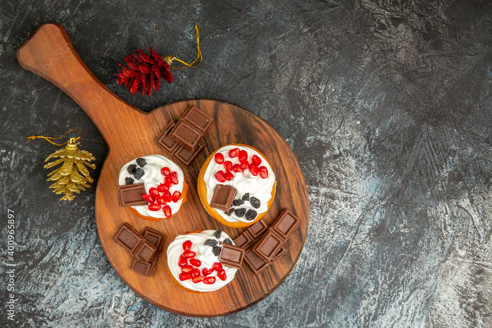 topt view berry cakes and chocolates on chopping board golden and red pinecones on grey-white background with copy space topt view berry cakes and chocolates on chopping board golden and red pinecones on grey-white background with copy space