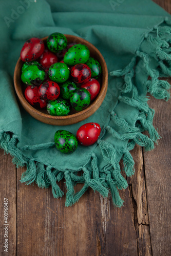 Easter colored eggs. Quail egg of green and red color on a wooden background. Willow branch. Happy Easter greeting card. Place for your text. Food on the background.